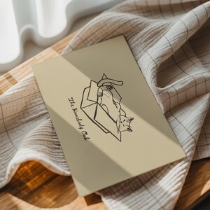 Minimal black line drawing of a cat lounging in a box, styled as a funny cat poster with homebody decor charm for a cozy book nook poster space, text reads “The Homebody Club”.