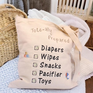 May include: A beige canvas tote bag with the text "Tote-ally Prepared" and a checklist of items including "Diapers", "Wipes", "Snacks", "Pacifier", and "Toys".