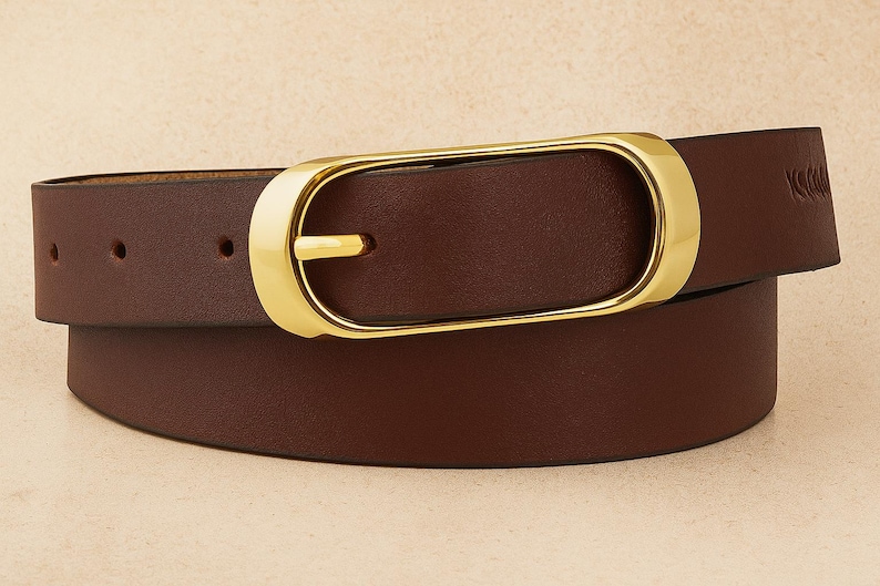 May include: A brown leather belt with a gold-colored oval buckle. The belt has a classic design with a single belt loop and several holes for adjustment. The belt is a versatile accessory.
