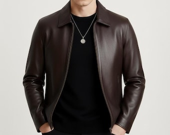 May include: A brown leather jacket with a collared neckline and a zipper closure. The jacket is worn over a black sweater and paired with black pants. A silver necklace hangs around the neck.