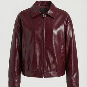 May include: A burgundy-colored, faux leather jacket with a collared neckline and a front zipper closure. The jacket has long sleeves, two side pockets, and a slightly oversized fit. The material has a glossy finish.