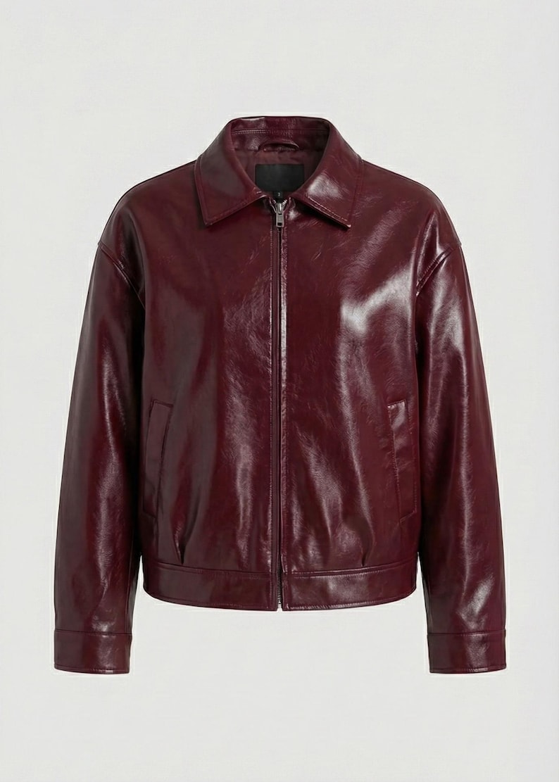 May include: A burgundy-colored, faux leather jacket with a collared neckline and a front zipper closure. The jacket has long sleeves, two side pockets, and a slightly oversized fit. The material has a glossy finish.