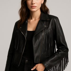 May include: A black leather jacket with fringe detailing. The jacket features a classic biker style with a notched collar, a zipper closure, and fringe accents along the chest and sleeves. The model is wearing a black top and black jeans.