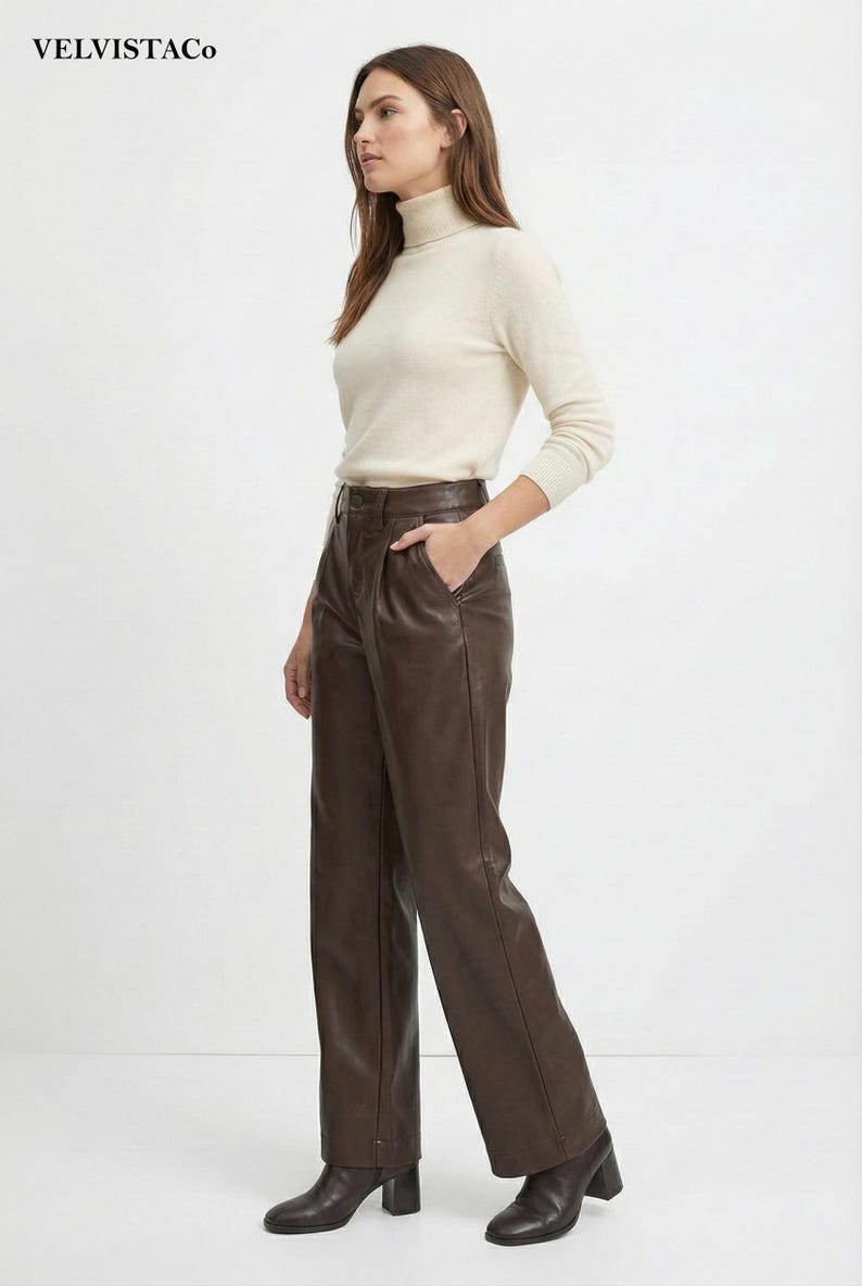 May include: A woman wearing a cream-colored turtleneck sweater and brown leather pants. The pants are high-waisted with a wide leg. The outfit is simple and elegant, suitable for various occasions. The brand name "VELVISTACO" is visible in the top left corner.