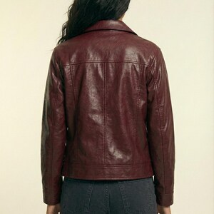 May include: A burgundy faux leather jacket with a classic collar and a tailored fit. The jacket features a button closure, pockets, and a structured silhouette. The back view showcases the jacket's design and stitching details. The brand name "VELVISTACO" is visible in the top left corner.