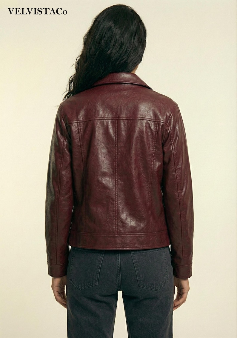 May include: A burgundy faux leather jacket with a classic collar and a tailored fit. The jacket features a button closure, pockets, and a structured silhouette. The back view showcases the jacket's design and stitching details. The brand name "VELVISTACO" is visible in the top left corner.