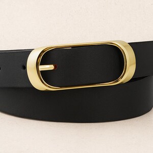 May include: A black belt with a gold-colored buckle. The buckle has a rectangular shape with rounded edges. The belt is made of a smooth, solid black material. The belt is curved, suggesting it is worn around the waist.
