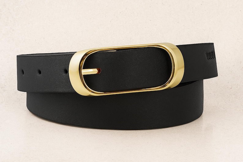 May include: A black belt with a gold-colored buckle. The buckle has a rectangular shape with rounded edges. The belt is made of a smooth, solid black material. The belt is curved, suggesting it is worn around the waist.