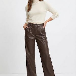 May include: A woman wearing a cream-colored turtleneck sweater and brown leather pants. The pants are wide-legged with a high waist. The outfit is simple and elegant, suitable for various occasions.