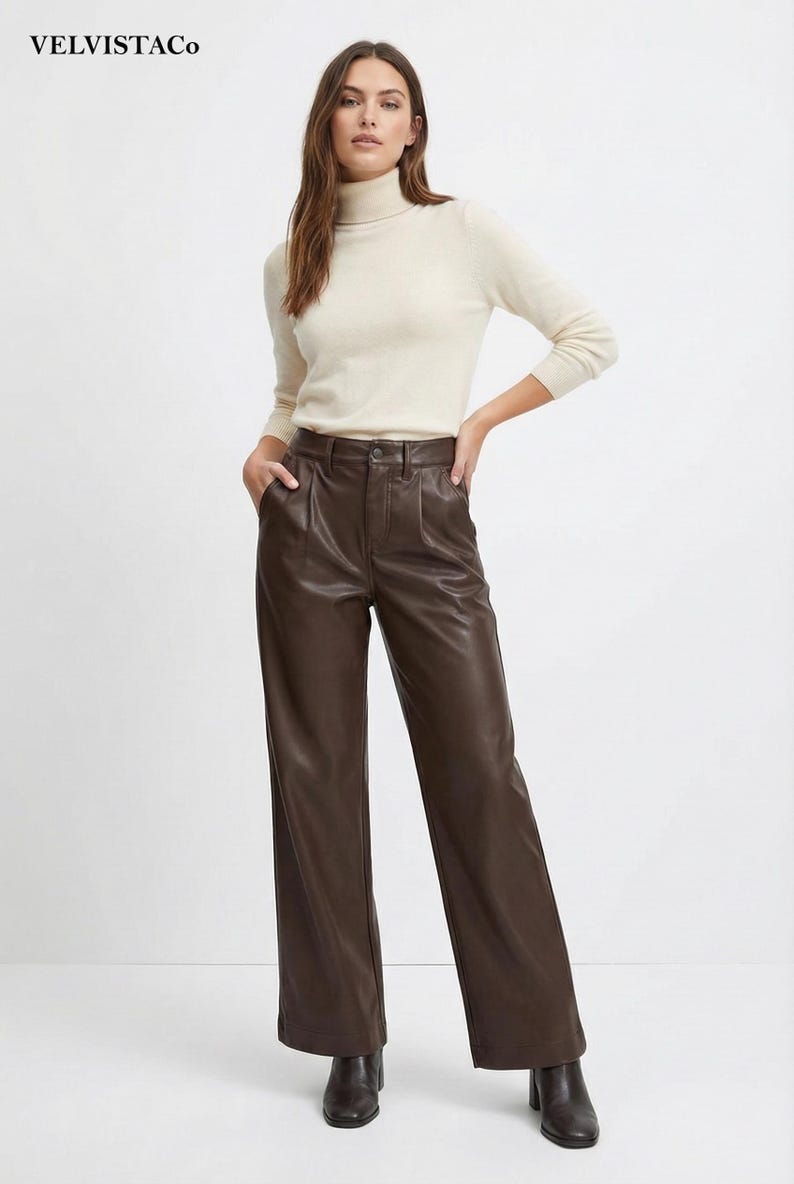 May include: A woman wearing a cream-colored turtleneck sweater and brown leather pants. The pants are wide-legged with a high waist. The outfit is simple and elegant, suitable for various occasions.