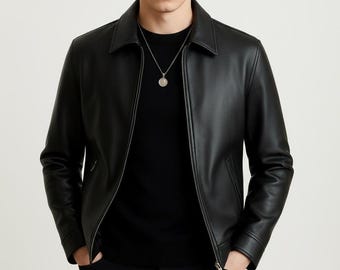 May include: Black leather jacket with a collar and a zipper closure. The jacket is worn over a black sweater and paired with black pants. A silver necklace with a pendant is visible. The brand name "VELVISTACO" is in the top left corner.