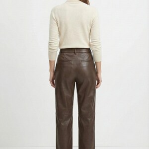 May include: A person is shown from the back, wearing a cream-colored turtleneck sweater and brown leather pants. The pants are high-waisted with a straight leg. The outfit is simple and classic, suitable for various occasions.
