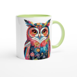 Könnte beinhalten: Weiße Keramiktasse mit einer bunten Eulenillustration. Die Eule hat leuchtende Farben wie Rot, Orange, Blau und Grün mit floralen und geometrischen Mustern. Die Tasse hat einen hellgrünen Henkel und Rand.