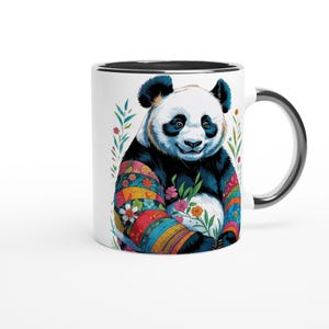 Peut inclure: Mug en céramique blanche avec un bord et une anse noirs. La tasse présente une illustration colorée d'un panda portant un pull à motifs et tenant des fleurs. Des motifs floraux entourent le panda.