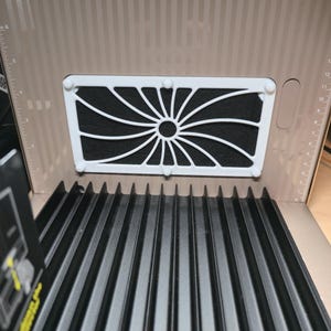 Puede incluir: Caja de cartón abierta con un filtro blanco con un diseño de sol. El filtro está sobre un fondo oscuro y texturizado. La caja tiene una base negra corrugada y un interior beige.