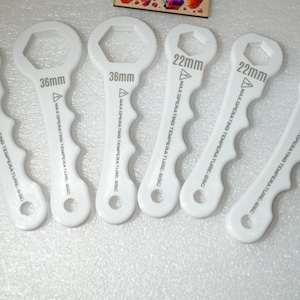 Könnte beinhalten: Sechs weiße Schraubenschlüssel in verschiedenen Größen, darunter 26mm und 36mm, sind abgebildet. Jeder Schraubenschlüssel hat eine sechseckige Öffnung und einen gebogenen Griff. Text auf den Schlüsseln zeigt die Größe und maximale Betriebstemperatur an.