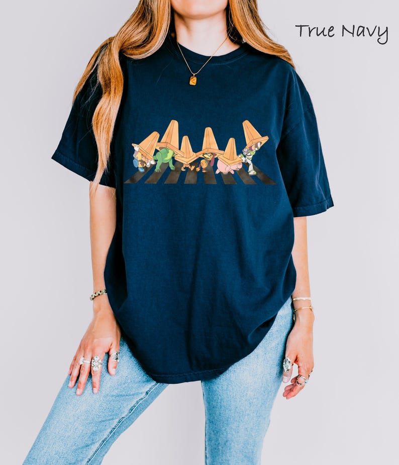 Puede incluir: Camiseta azul marino con un gr&aacute;fico de dibujos animados de personajes cruzando un paso de cebra, con conos de tr&aacute;fico encima. El texto "True Navy" est&aacute; escrito en cursiva. La camiseta es de corte holgado.