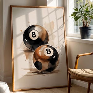 Puede incluir: Un cuadro enmarcado con dos bolas de billar estilizadas con el número 8 en blanco. Las bolas son negras, marrones y blancas. La obra de arte tiene un efecto acuarela y se exhibe en una habitación bien iluminada.