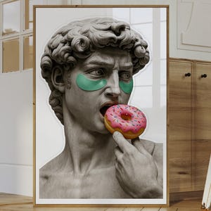 May include: A framed print featuring a classical sculpture of David with green eye patches and a pink donut in his mouth. The artwork is displayed in a well-lit room with other framed art and furniture.