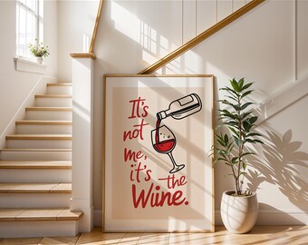 May include: A framed art print with the text "It's not me, it's the Wine." The artwork shows a wine bottle pouring into a wine glass. The print is displayed in a bright room with a staircase and a potted plant, creating a welcoming atmosphere.