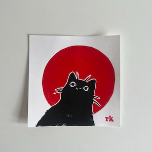 Könnte beinhalten: Quadratischer Druck mit einer schwarzen Katzen-Silhouette vor einem roten Kreis, der an eine aufgehende Sonne erinnert. Die Katze hat weiße Schnurrhaare und Augen. Die Initialen "rk" befinden sich unten rechts. Das Kunstwerk ist auf weißem Papier.
