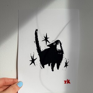 May include: Black and white art print of a screaming cat with star accents. The cat is silhouetted against a white background. The artist's initials, "rk", are in red in the lower right corner.