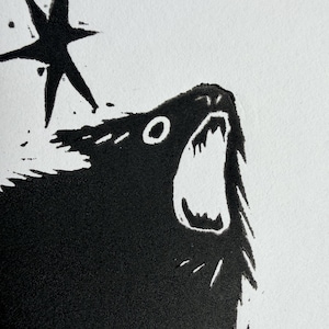 May include: A black and white linocut print featuring a howling wolf with an open mouth and a five-pointed star. The artwork has a textured appearance and is set against a white background.