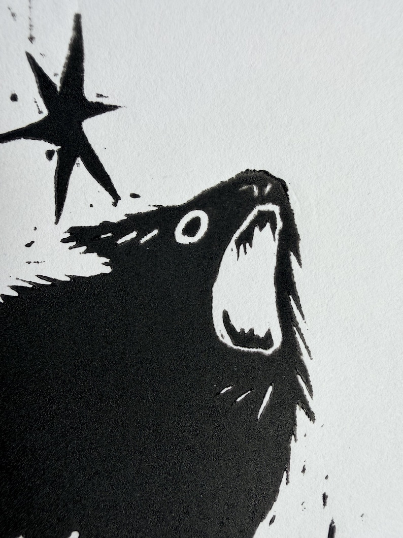 May include: A black and white linocut print featuring a howling wolf with an open mouth and a five-pointed star. The artwork has a textured appearance and is set against a white background.