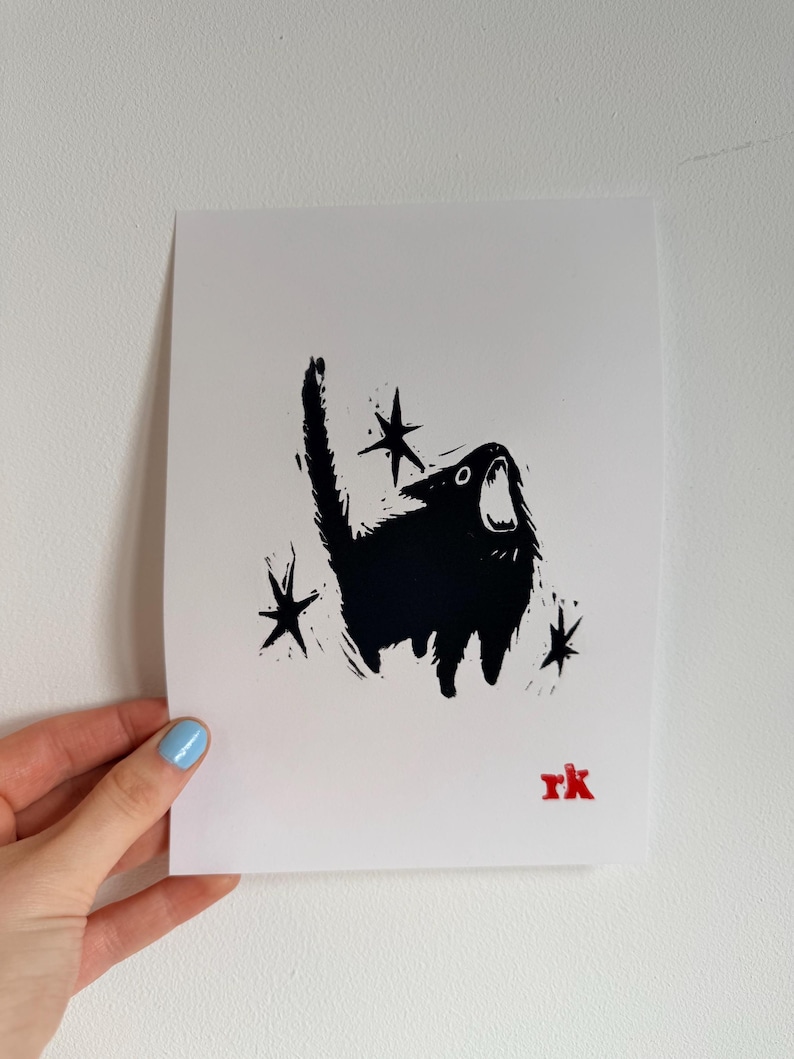 May include: Black and white art print featuring a stylized black cat with an open mouth, surrounded by star shapes. The cat has a textured appearance. The artist's initials, "rk", are in red in the lower right corner.