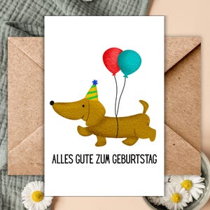 Op de afbeelding: Een verjaardagskaart met een cartoon teckel met een feesthoedje en twee ballonnen. De ballonnen zijn rood en blauwgroen. De kaart heeft de Duitse zin "Alles Gute zum Geburtstag" erop gedrukt.