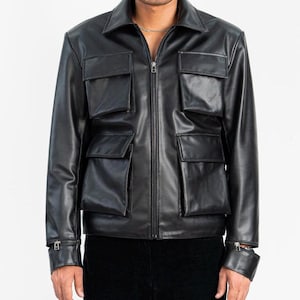 Pode incluir: Casaco de couro preto com gola, fecho de correr frontal e vários bolsos frontais. O casaco tem um corte sob medida e punhos ajustáveis com fechos de botão. Uma peça de roupa exterior clássica e versátil.