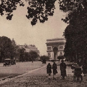 May include: Vintage sepia-toned postcard featuring a Parisian street scene. The Arc de Triomphe is visible in the background, with trees lining the road and vintage cars. Several people are walking along the road.