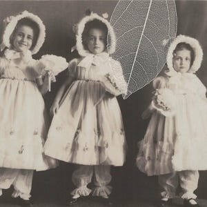 Carte postale vintage des années 1920 : trois petites filles habillées de la même manière avec des bonnets, des robes à volants et des pantalons, édition privée