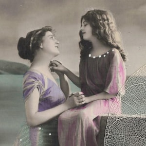 May include: Vintage sepia-toned photograph featuring two women in flowing gowns. One woman, in a purple dress, looks up at the other, who is in a pink dress. The background shows a landscape with a body of water and a cloudy sky.