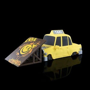 Puede incluir: Un taxi de juguete amarillo con la palabra "TAXI" en la parte superior, junto a una rampa de madera marrón con una cara sonriente y la palabra "SKATE" en ella.