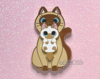 May include: A gold enamel pin depicting a brown and white Siamese cat holding a smaller white Siamese kitten. The pin has a glossy finish and is a cute and whimsical design.