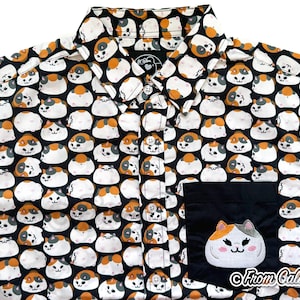 May include: Black button-up shirt with a repeating pattern of cartoon cats in white, orange, and gray. The shirt features a black pocket with an embroidered cat face and the text "From Caliko".
