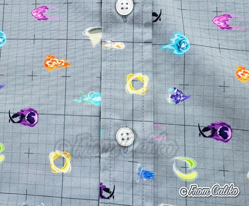 Puede incluir: Primer plano de una camisa gris con botones con un patr&oacute;n de cuadr&iacute;cula y explosiones de energ&iacute;a coloridas y de dibujos animados. Las explosiones son en tonos naranja, morado, azul y amarillo. La camisa tiene botones blancos y el texto "From Caliko".