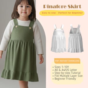 May include: A child wearing a green pinafore dress over a white top. The dress features buttoned straps and a frilled hem. The image includes a diagram of the dress and text that reads "Pinafore Skirt" and "Easy to sew - Perfect for Beginner."