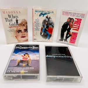 May include: Five cassette tapes with clear plastic cases. The tapes are labeled with the titles "Madonna Who's That Girl", "Beverly Hills Cop", "Pretty Woman", "Even Cowgirls Get the Blues", and "Soundtrack from Thirtysomething".