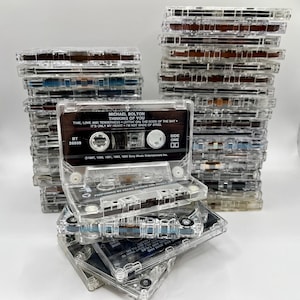 May include: A stack of clear cassette tapes with a Michael Bolton cassette tape on top. The cassette tape is labeled "Thinking of You" and features the song titles "Time, Love and Tenderness", "Sitting on the Dock of the Bay", and "It's Only My Heart - I'm Not Made of Steel".