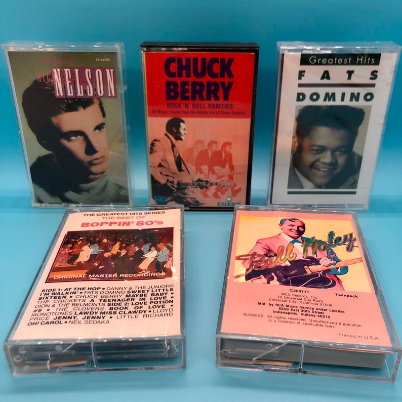 Puede incluir: Cinco cintas de cassette con portadas coloridas que muestran a m&uacute;sicos como Chuck Berry, Fats Domino y Bill Haley. Las cintas est&aacute;n etiquetadas con el nombre del artista y el t&iacute;tulo del &aacute;lbum. Las cintas est&aacute;n dispuestas en una fila sobre una superficie azul.