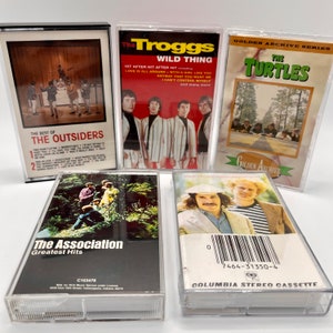 May include: Five cassette tapes featuring different band names and album titles. The tapes are all in clear plastic cases. The tapes are from the 1960s and 1970s. The bands are The Outsiders, The Troggs, The Turtles, The Association, and a tape with no band name.