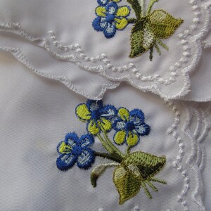 Puede incluir: Dos servilletas de tela blanca con flores bordadas azules y amarillas. Las servilletas tienen bordes festoneados y est&aacute;n superpuestas. La fecha 08/21/2018 est&aacute; escrita en la esquina inferior derecha.