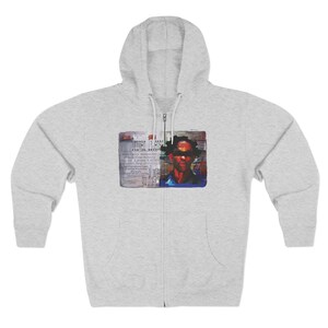 May include: A light grey zip-up hoodie with a hood and a front pocket. The hoodie features a graphic on the front with the text "DRIVER IN EGO" and a portrait of a person with sunglasses.