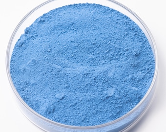 May include: A clear glass petri dish filled with a fine, light blue powder. The powder has a uniform texture and fills the dish completely. The dish is set against a white background.