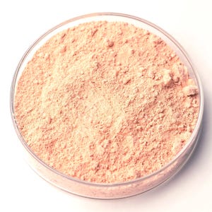 Può includere: Un piatto rotondo di vetro trasparente riempito con una polvere color pesca chiaro. La polvere ha una consistenza fine e granulosa e sembra essere distribuita uniformemente nel piatto. Il piatto è posto su uno sfondo bianco.