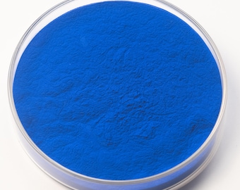 May include: A petri dish containing a vibrant, deep blue powder. The powder fills the circular dish, creating a textured surface. The dish is made of clear glass, and the background is plain white.