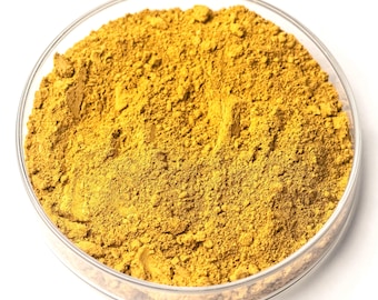 May include: A clear, round glass dish filled with a vibrant yellow powder. The powder has a fine, granular texture and appears to be evenly distributed within the dish. The background is plain white, highlighting the color and texture of the powder.