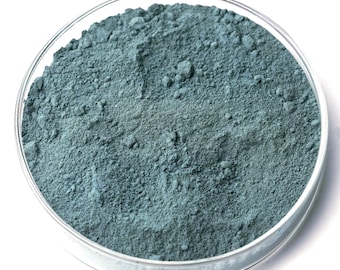 Könnte beinhalten: Eine transparente Petrischale aus Glas, gefüllt mit einem teal-farbenen Pulver. Das Pulver hat eine feine, körnige Textur und ist gleichmäßig in der Schale verteilt. Der Hintergrund ist schlicht weiß und bildet einen Kontrast zum Pulver.